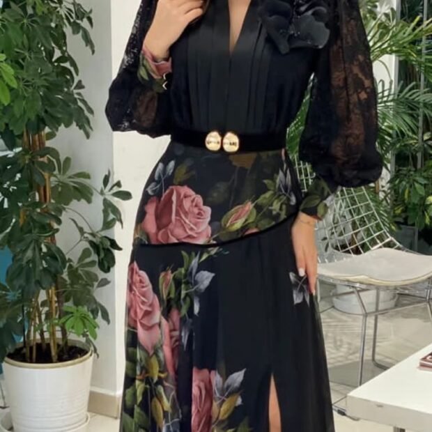 This elegant black maxi dress features sheer lace bishop sleeves and a sophisticated pleated V-neck bodice adorned with a tonal floral accent on the shoulder. A velvet waist belt featuring double metallic statement buttons defines the figure. The flowing skirt showcases a vibrant vintage rose floral print and a high front slit